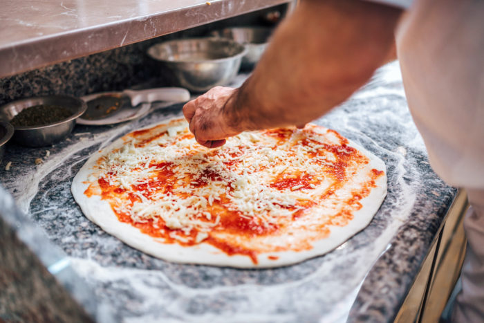 Chef making the pizza. Close-up. Adding cheese on pizza base.